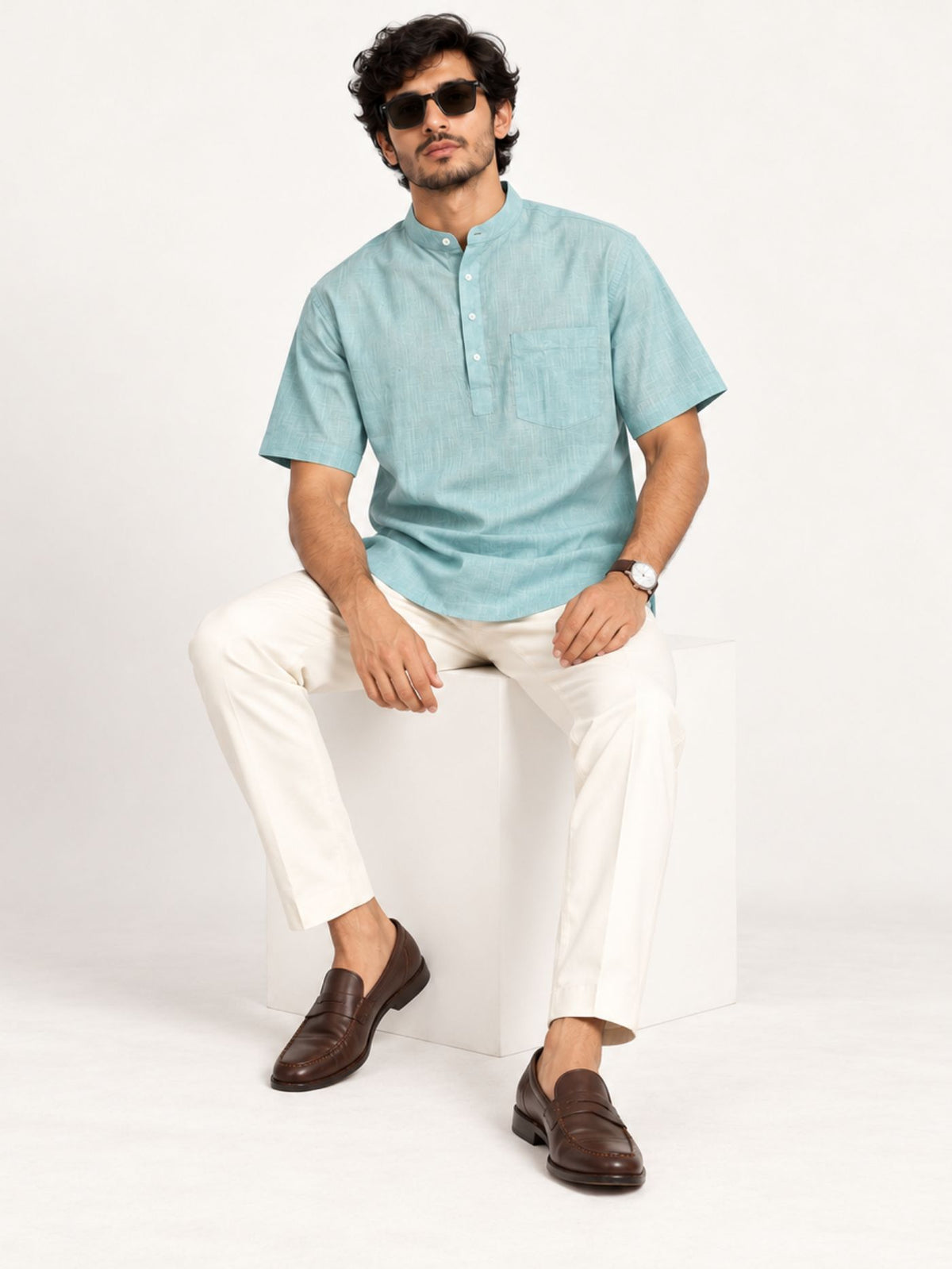 Seated model wearing Aavir seafoam blue half sleeve kurta shirt with ivory trousers