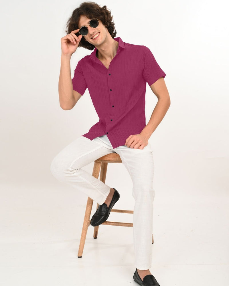 Man sitting in magenta shirt with white pants.