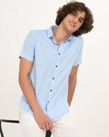 Man wearing Skyline Blue short-sleeve textured shirt, leaning on chair.