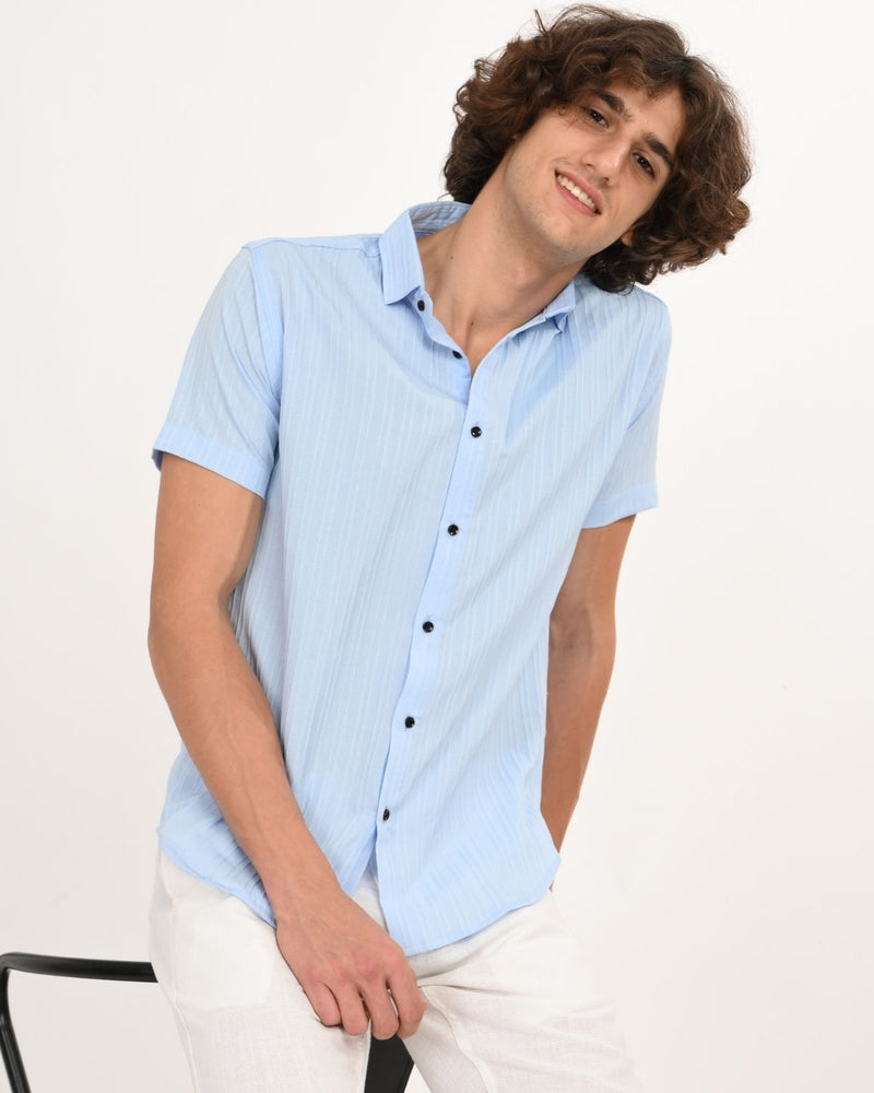 Man wearing Skyline Blue short-sleeve textured shirt, leaning on chair.