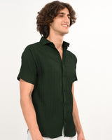 Man wearing a dark green textured short-sleeve shirt, side pose with a smile.