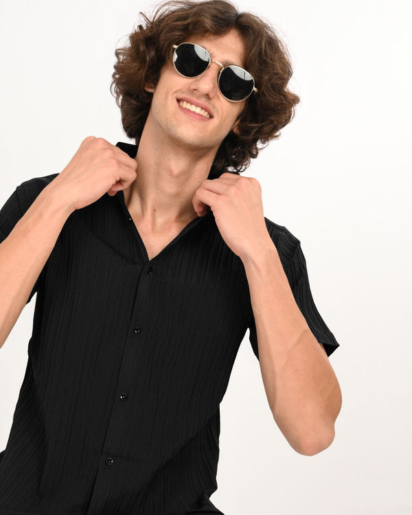 Man wearing black textured short-sleeve shirt adjusting collar
