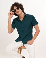 Model sitting wearing teal green short-sleeve shirt with sunglasses
