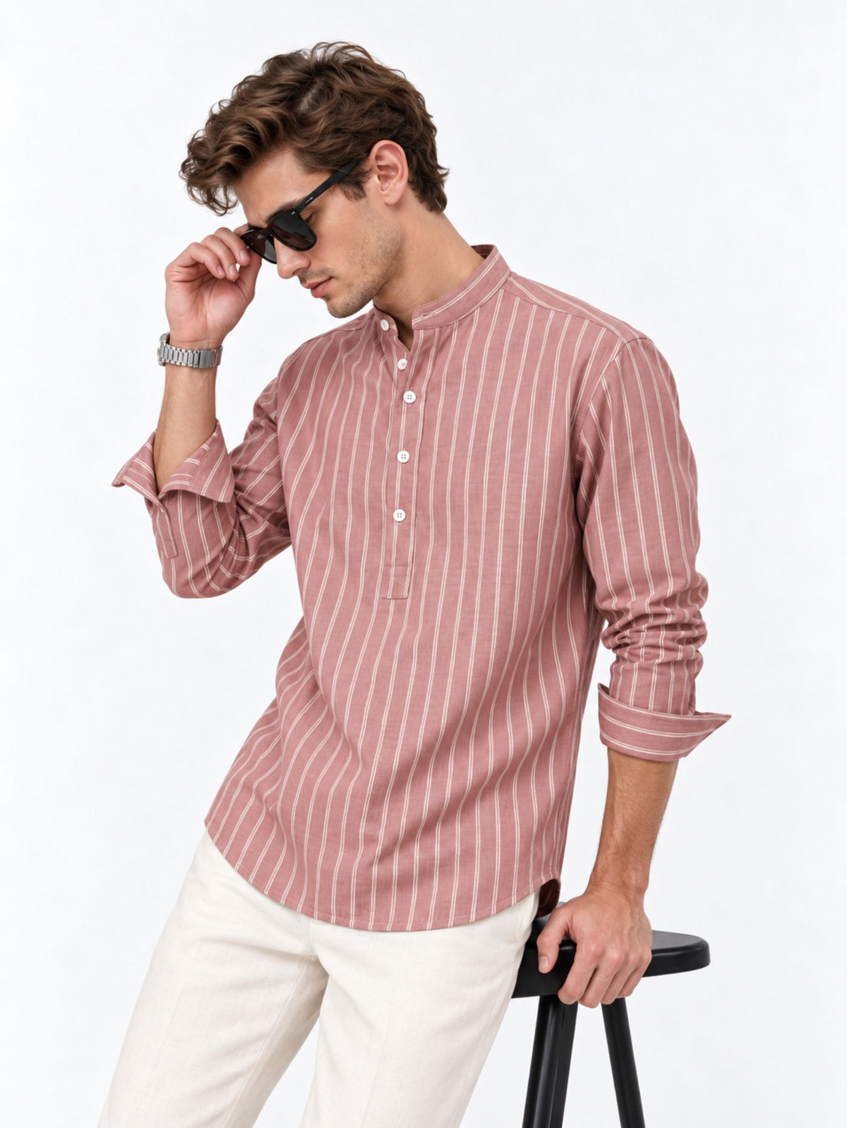 Model wearing Veer Muted Rose striped kurta shirt with rolled sleeves, leaning against a black stool.